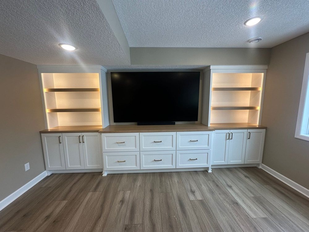 A finished basement in Chanhassen, MN with a wall-mounted TV, white built-in cabinetry, and open shelving by BN Builders.