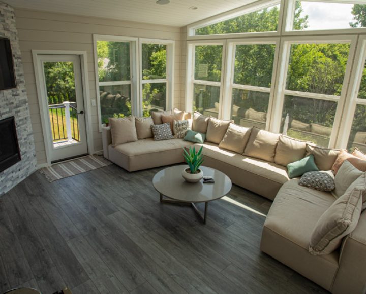 A serene enclosed patio featuring comfortable seating, a modern fireplace, and large windows that provide a view of the lush green surroundings.