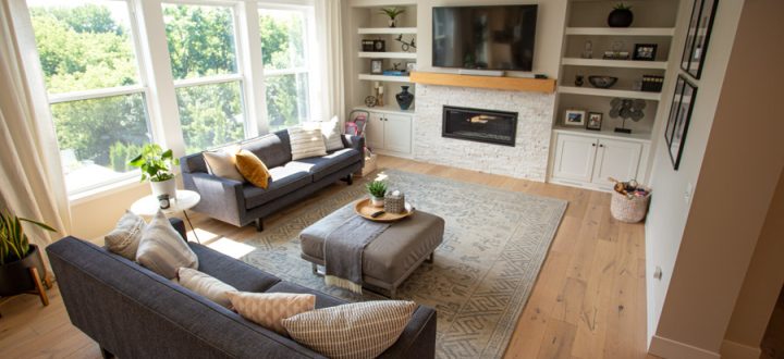 A beautifully designed family room with a stone fireplace, built-in shelving, and plush seating, highlighted by large windows and warm wooden flooring.