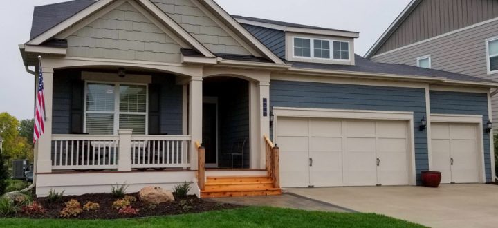 A charming home renovation featuring a new wooden front porch and a fresh exterior, complete with an American flag and landscaped garden.