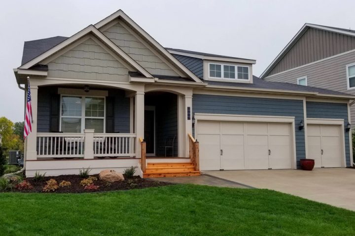 A charming home renovation featuring a new wooden front porch and a fresh exterior, complete with an American flag and landscaped garden.