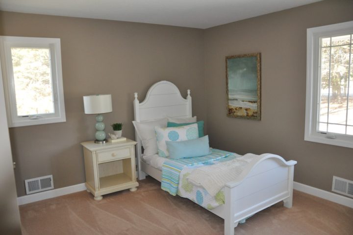 A child's bedroom featuring a white sleigh bed with blue and green bedding, a light wood nightstand, and coastal-themed artwork on the walls.
