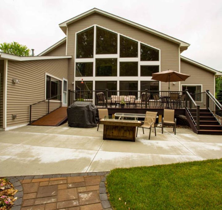 The back of a beige home featuring a large concrete patio, a fire pit table, outdoor seating, and a multi-level deck with large windows.
