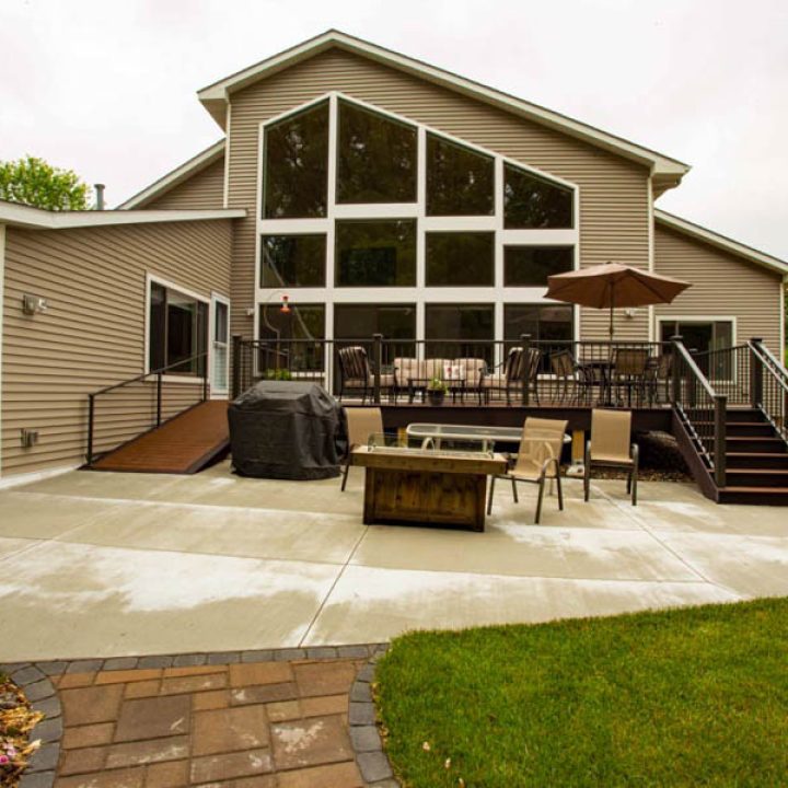 The back of a beige home featuring a large concrete patio, a fire pit table, outdoor seating, and a multi-level deck with large windows.
