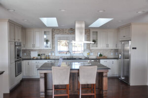 A kitchen featuring cream-colored cabinets, a stone tile backsplash, a large island with bar stools, and stainless steel appliances.
