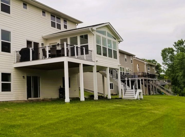 A line of contemporary homes with white siding and large upper decks, each supported by white posts and connected by stairs, overlooking a well-maintained green lawn.