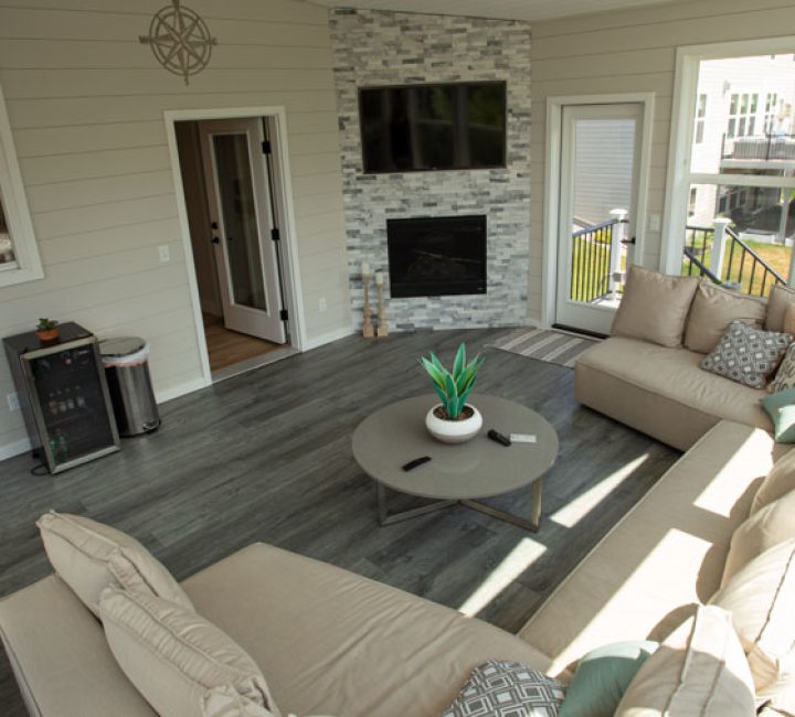 A cozy screened porch featuring a stone fireplace with a wooden mantel, wicker furniture, and decorative lanterns on the hearth.