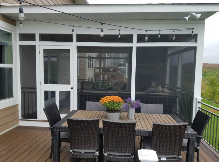 A white-framed screened porch with a dark wicker dining set, vibrant flower centerpiece, and string lights hanging from the ceiling.