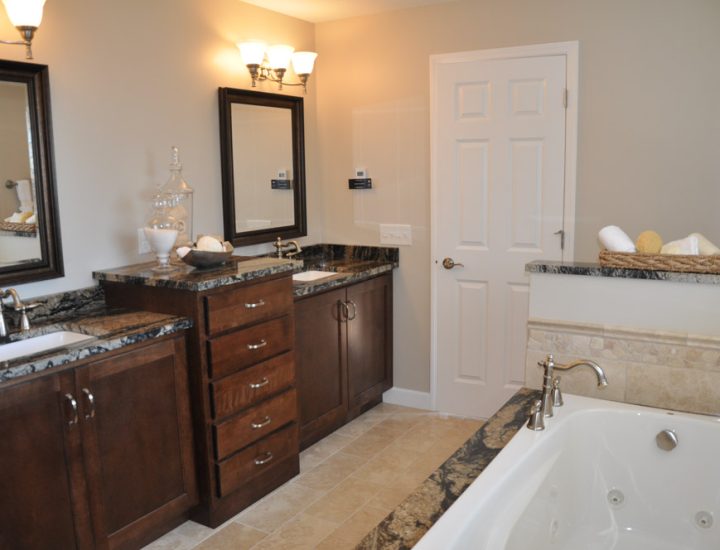 A classy bathroom with tub in a granite deck, a wood cabinets with granite countertops and sinks