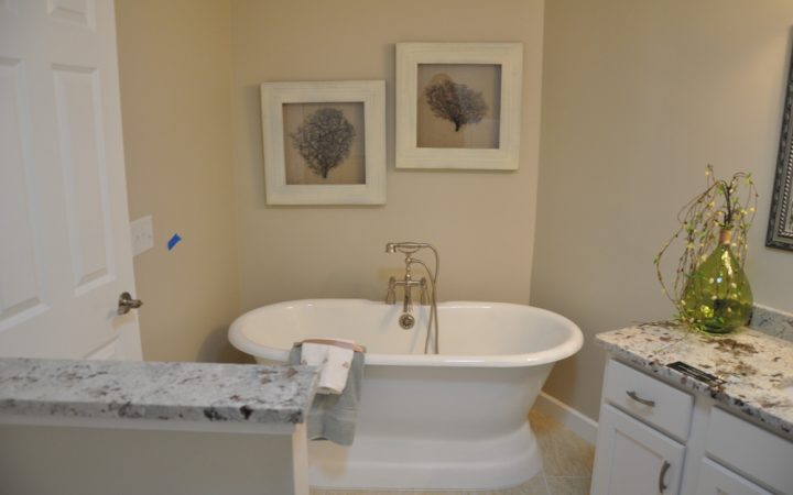 A freestanding bathtub in a bathroom, with art wall displays, marble countertops and white cabinets