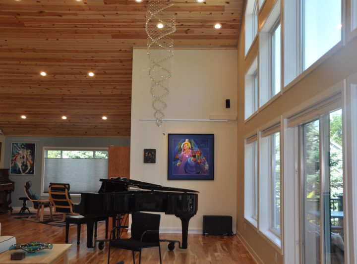 Artistic hanging lights from a wood plank ceiling of a living room with a piano, and a wall art display